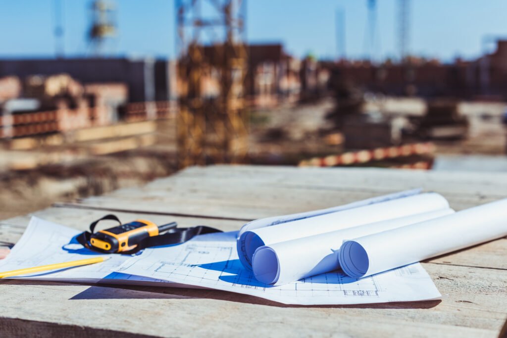 rolls of paper with building plans and portable radio on wooden surface at construction site